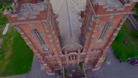 A-beautiful-old-Church-top-close-up-aerial-view,-Red-building-of-the-Church,-Green-trees-and-grass-around-the-Church,-Cross-at-the-top-and-bottom-of-the-Church