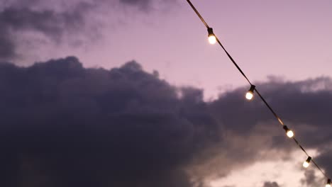 String-of-glowing-outdoor-party-lights-against-a-beautiful-sunset-sky-at-dusk