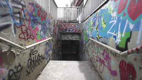Dolly-forward-through-stairs-leading-to-a-tunnel-with-graffiti-on-walls