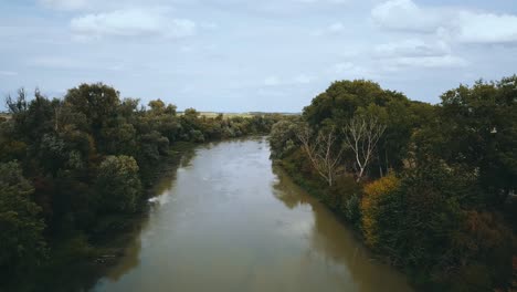 Drone-shot-of-muddy-slow-river-between-fields-and-trees