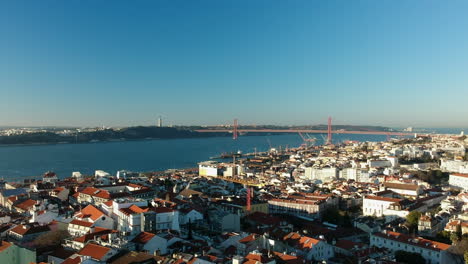 Aerial-dolly-forward-above-the-city-of-Lisbon-with-Ponte-25-de-Abril-and-Cristo-Rei-in-the-backgrund,-Lisbon,-Portugal