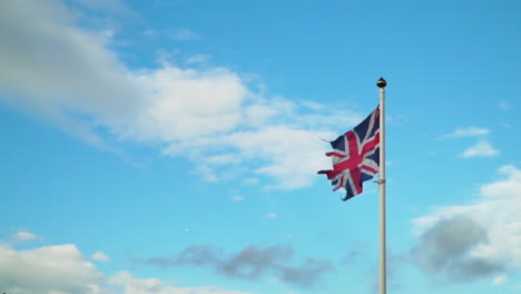 Old-Ripped-Union-Jack-Flag-Blowing-in-Slow-Motion-Against-Blue-Sky