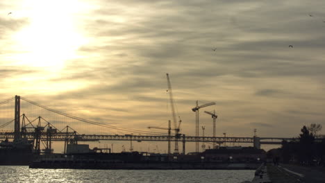 25Th-April-Bridge-in-the-sunset-with-road-traffic,-construction-cranes-and-Tejo's-River