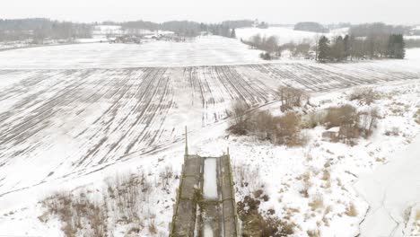 Aerial-view-of-abandoned-bridge-and-agricultural-field-during-winter