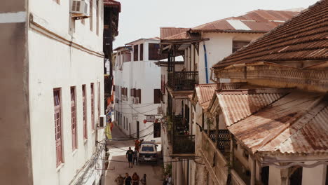 Old-narrow-street-of-Zanzibar-Stone-Town-with-cars-parked-on-the-sides-of-the-road-and-tourist-and-local-walking-in-the-street