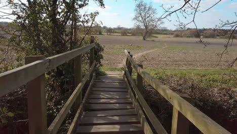 Man-made-wooden-footbridge-over-shallow-stream-leading-into-barren-farmers-field
