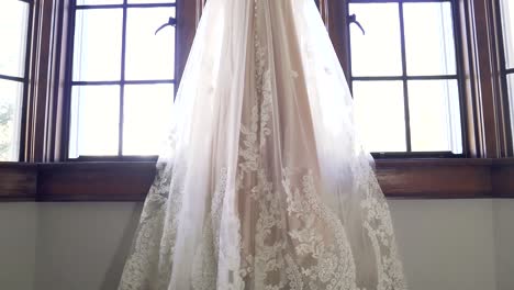 Slow-Motion-Reveal-Of-Elegant-Wedding-Dress-Hanging-In-Window-Frame,-Backless-Design,-White-Wedding-Gown,-Pearl-Accents