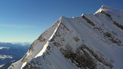 Aerial-view-rising-up-a-mountain-ridge-in-the-French-Alps-in-winter-with-sun-shine