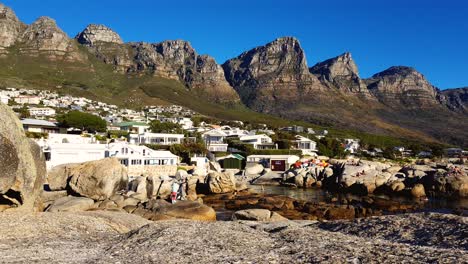Static-shot-of-holiday-homes-at-the-base-of-mountainous,-rocky-South-African-apostles-range-with-seascape-below