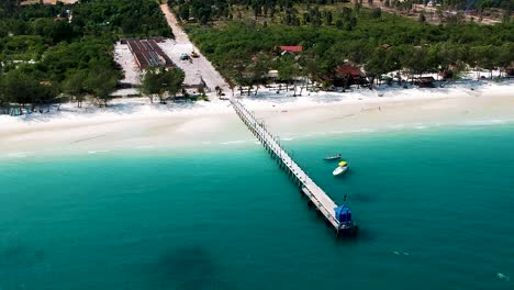 Aerial-of-beautiful-white-sand-beach-with-wooden-pier-and-turquoise-blue-sea