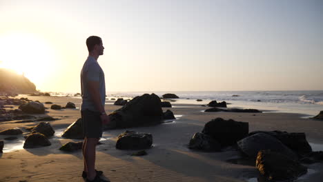 A-strong-and-fit-young-man-watching-the-ocean-waves-and-preparing-for-a-morning-run-on-the-beach-at-sunrise-in-Santa-Barbara,-California