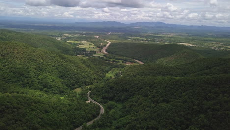 Aerial-view-of-countryside-road-passing-through-the-lush-greenery-and-foliage-tropical-rain-forest-mountain-landscape