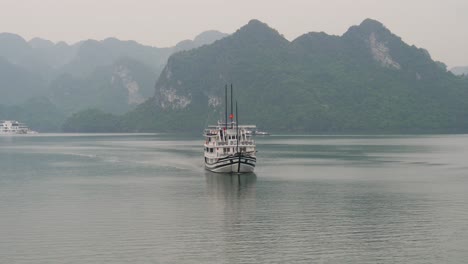 Ship-cruising-in-Halong-Bay-while-other-boats-are-anchored-with-misty-horizon