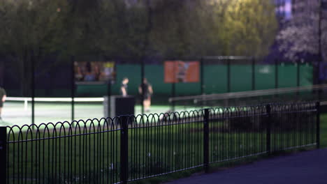 Gente-Jugando-Tenis-En-La-Distancia,-Noche-En-King-George&#39;s-Park,-Londres,-Reino-Unido
