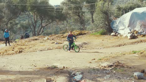 Lindo-Joven-Caminando-Su-Bicicleta-Verde-Brillante-En-Un-Campo-De-Refugiados-En-Grecia