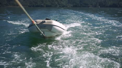 Inflatable-boat-being-towed-on-rope-behind-boat-on-sea-of-New-Zealand