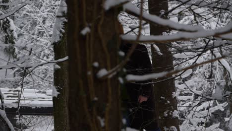Young-east-european-men-walks-through-the-snowy-woods-in-winter-clothes-with-his-black-camera