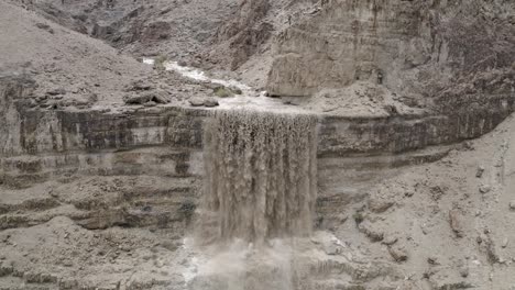 Powerful-waterfall-aerial-close-up,-Israeli-desert,-flood-water-after-rain,-pull-out-drone-shot