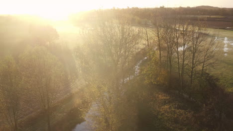 Aerial-view-descending-alongside-the-river-Stour,-Kent,-UK-with-a-stunning-sunrise-illuminating-the-mist