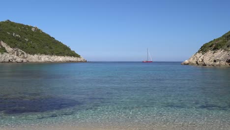 Smooth-reveal-shot-of-the-clear-waters-of-Porto-Timoni-beach-with-a-sailing-yacht-complementing-the-scene