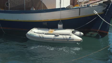 Small-plastic-dinghy-tied-to-larger-carvel-built-wooden-sail-boat-in-harbor