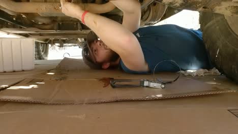Static-shot-of-a-man-lies-under-truck-doing-repairs-on-a-bright-hot-day