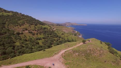 Aerial:-Unpaved-road-on-the-cliffs-of-Lesbos-with-2-scooters-driving-down