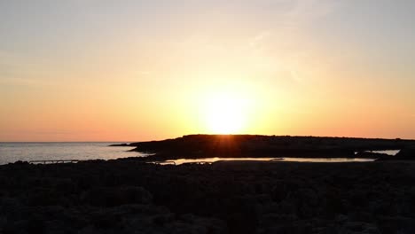 Sonnenaufgang-Auf-Den-Steinen-Vor-Dem-Meer,-Der-Den-Sonnenaufgang-Hinter-Einer-Kleinen-Insel-Einfängt