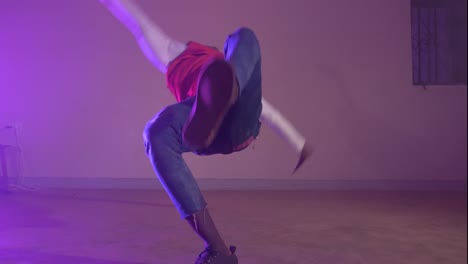 Slow-motion-shot-of-African-youth-in-a-red-shirt-twisting-his-body-on-his-hands-while-break-dancing-in-colorful-lights