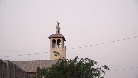 Church-steeple-and-statue-during-sunset-in-La-Molina,-Lima,-Peru-PANNING-FROM-RIGHT-TO-LEFT
