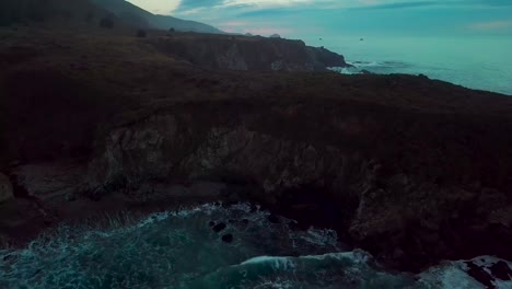 Fast-dolly-out-reveal-of-huge-ocean-cliffs-and-crashing-waves-at-Sand-Dollar-Beach-at-dusk-in-Big-Sur-California