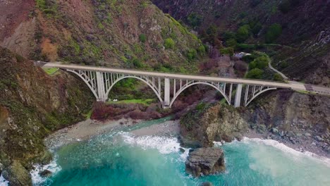 Aerial-pullback-view-of-Bixby-Creek-Bridge-and-Pacific-Ocean-with-surrounding-hills-in-Big-Sur-on-State-Route-1-in-California