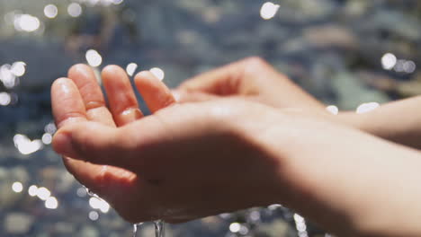 Close-up-of-woman's-hands-being-washed-in-a-clear-river-on-a-sunny-day