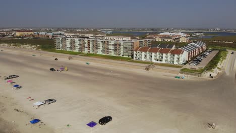 Rising-above-the-beach-diagonally-pointed-towards-lodging,-showing-vehicles-parked-on-beach,-several-entering-beach-access-road