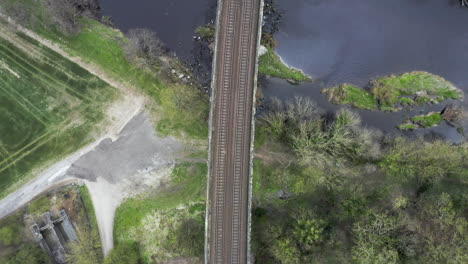 Aerial-Birds-Eye-View-of-Train-Tracks-Crossing-River-in-Yorkshire,-England-with-Ducks-Landing-in-Water