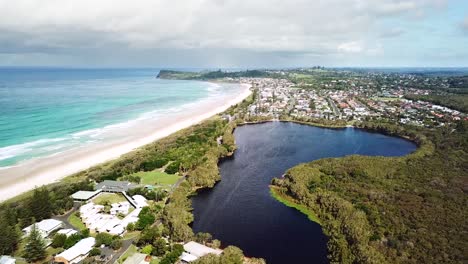 Drone-flying-in-sideways-arc-showing-freshwater-tea-tree-stained-lake,-adjacent-beach-and-headland-in-background