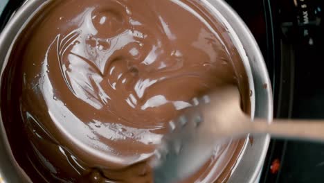 top-view-into-melting-pot-of-milk-chocolate-candy-rounds-being-stirred-with-spoon-as-they-completely-melt