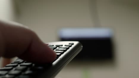 Hand-closeup-of-the-man-with-the-remote-control-and-watching-the-television-with-presses-to-change-the-channel-on-the-button