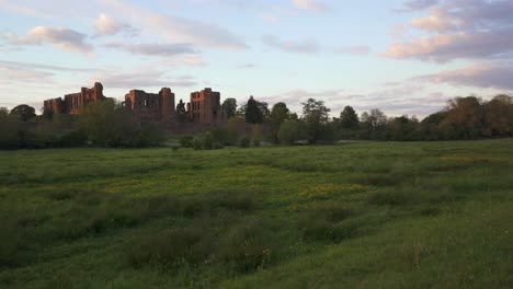 Langsamer-Schwenk-über-Die-Felder,-Der-Die-Ruinen-Von-Kenilworth-Castle-Zeigt,-Die-In-Das-Warme-Abendsonnenlicht-Getaucht-Sind
