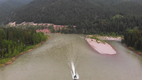 Aerial-shot-of-a-boat-speeding-up-Flathead-River,-in-Montana-wilderness,-drone-passes-over-boat-until-it's-no-longer-visible