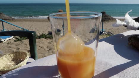 Pouring-juice-in-a-glass-on-the-beach-with-a-sea-view,-Marbella-Spain