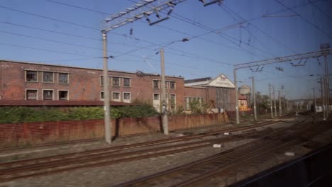 Langsam-Fahrender-Zug-Fährt-Die-Gleise-Hinunter-Und-Blickt-Aus-Dem-Fenster-Auf-Ein-Altes,-Heruntergekommenes-Industriegebäude