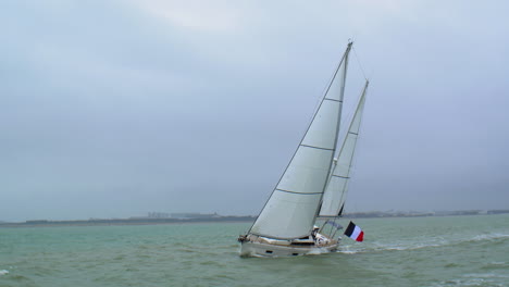 Sailing-vessel-yacht-with-French-flag-sailing-in-breaking-waves-and-healing-over