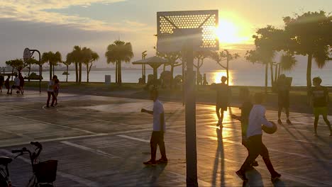 Teenager-Spielen-Basketball-Auf-Den-Plätzen-Am-Meer,-Im-Hintergrund-Blendet-Die-Sonne