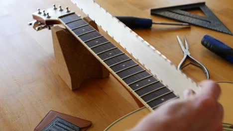Hands-of-a-luthier-craftsman-measuring-and-leveling-an-acoustic-guitar-neck-and-fretboard-on-a-wood-workshop-bench-with-lutherie-tools