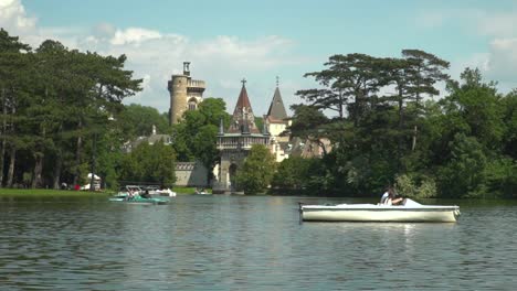 View-of-Laxenburg-castle-behind-lake-with-boats-passing-in-foreground-on-bright-and-sunny-summer-day