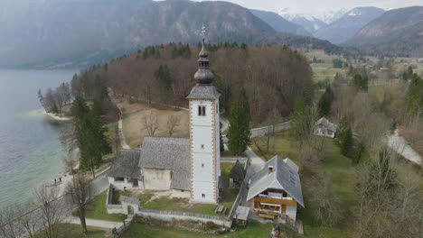 Point-of-drone-view-around-bridge-and-church-from-the-Bohinj-lake,-Slovenia