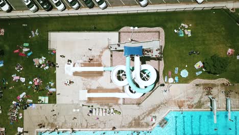 Lowering-drone-shot-directly-above-a-large---twisty-double-waterslide-at-an-outdoor-public-pool