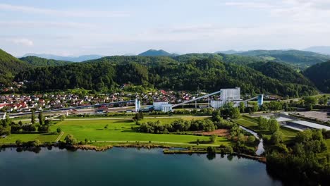Luftaufnahme-Einer-Industriefabrik-Und-Der-Küste-Eines-Sees-Mit-Hügeln-Im-Hintergrund-In-Der-Nähe-Von-Velenje,-Slowenien,-Europa