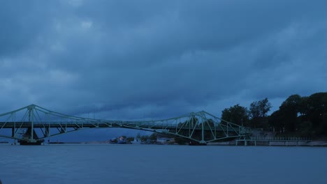 Time-lapse-of-beautiful-fast-moving-dark-gray-rain-clouds-over-the-Oskara-Kalpaka-swing-bridge-in-Liepaja-city-in-evening,-wide-shot
